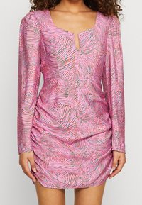 Vaaleanpunainen pitkähihaiset mekko, jossa on syvä V-pääntie ja kieppumalli eri väreissä. Kankaassa on hieman kiiltoa ja joustavaa rypytystä vyötäröllä.