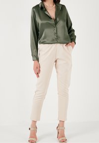 Olive green satin blouse with a collar, paired with beige tapered pants and beige heels. The blouse has a button-up front and long sleeves.