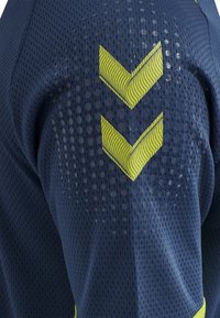 Marineblauw netstof sporttrui met gele chevronpatronen. Textuur oppervlak en ademend ontwerp verbeteren ventilatie en comfort.