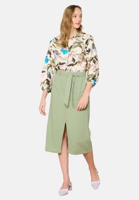 Gėlių ilgaaulių rankovių blusas pastelinių spalvų, su susiraukšlėjusiomis rankovėmis, derinamas su šviesiai žaliu sijonu su priekine iškirpte ir surišamu juosmeniu.
