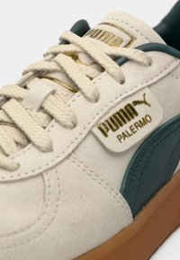 Sneaker featuring a white suede upper, teal leather accents, and a gold logo tag. Round laces and a gum rubber sole complete the design.