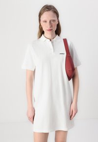 Biela polo šaty s golierom a krátkymi rukávmi, s malým čiernym logom "2NDAY". Modelka nesie červenú crossbody tašku.