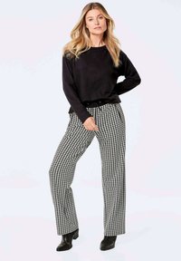 Schwarzer Langarmpullover kombiniert mit hoch taillierten Hosen im Hundezaun-Muster. Schwarze Stiefeletten runden das Outfit ab.