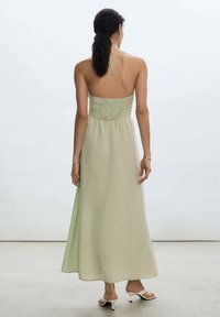 Robe maxi verte claire avec un corsage smocké et un col halter. Tissu doux et fluide avec une texture lisse, atteignant jusqu'aux chevilles.