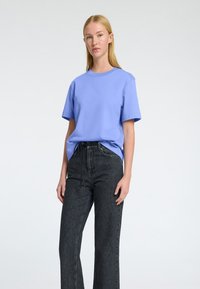 T-shirt en coton bleu clair à manches courtes, associé à un pantalon en denim noir taille haute. La tenue présente une coupe décontractée et des détails minimalistes.