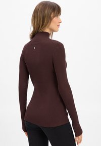 Brązowy sweter prążkowany z wysokim kołnierzem, z długimi rękawami i bocznym rozcięciem u dołu. Mały detal logo na tylnym dekolcie.