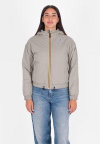 Giacca trapuntata grigia chiara con vita aderente, cappuccio e zip a contrasto gialla e nera. Presenta polsini elastici e orlo regolabile con cordino.