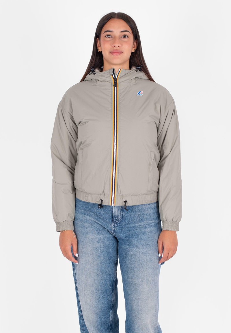 Giacca trapuntata grigia chiara con vita aderente, cappuccio e zip a contrasto gialla e nera. Presenta polsini elastici e orlo regolabile con cordino.