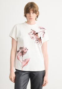 Witte katoenen t-shirt met korte mouwen, voorzien van roze bloemen- en vlinderprints aan de linkerzijde, ronde halslijn, en een relaxte pasvorm.
