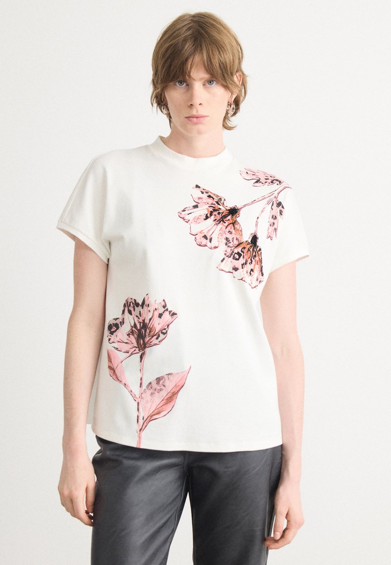 Witte katoenen t-shirt met korte mouwen, voorzien van roze bloemen- en vlinderprints aan de linkerzijde, ronde halslijn, en een relaxte pasvorm.