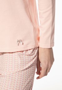 Lichtroze langemouwen top met een zilveren lintdetail aan de zoom, gecombineerd met roze broek met een bladerenpatroon in subtiele tinten.