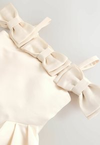 Kreemikarva ehk kleit, millel on kolm suurt lipsu õlgadel, pehme kangast tekstuur ja plekitud disain altpoolt.