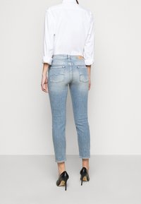 Jeans ajustados de color azul claro con cintura alta, desvanecimiento sutil y bolsillos traseros. Combinados con una camisa blanca de botones y tacones negros.