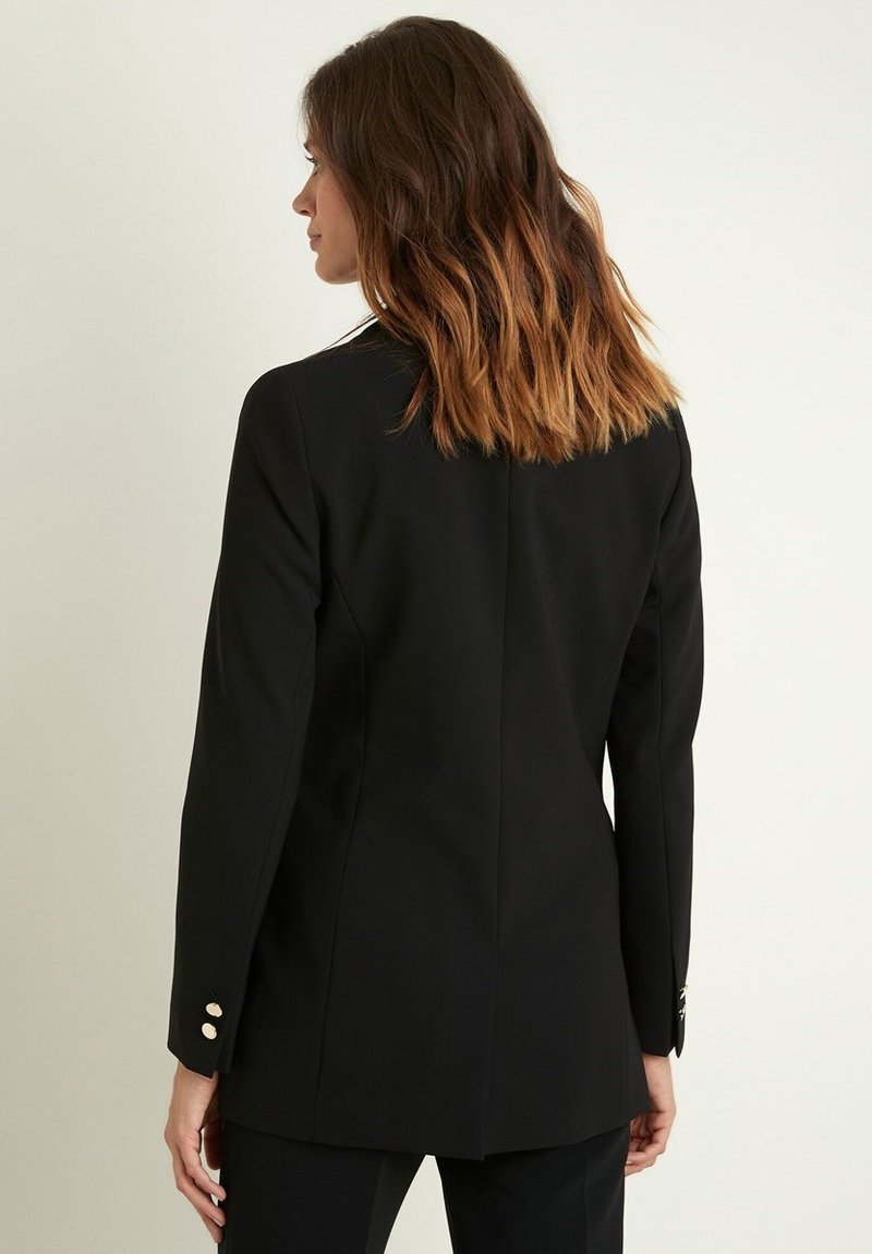 Blazer nero aderente realizzato in tessuto liscio, con una fessura posteriore singola e dettagli in bottone dorato sulle maniche.