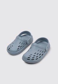 Helleblaue Clogs mit durchbrochenem Muster und verstellbarem Riemen. Glattes Gummi-Material und runde Zehenform. Flache Sohle.