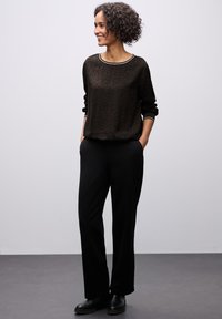 Top a maniche lunghe con stampa leopardata nera, scollo tondo e bordi a contrasto, abbinato a pantaloni neri a gamba larga e scarpe basse.