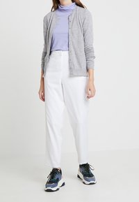 Grå kardan över en lavendelfärgad polotröja, parat med vita tapered byxor och flerfärgade sneakers med tjock sula.