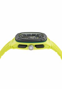 Négyzet alakú óra fekete számlappal és fehér jelzésekkel, lime-zöld szilikon házban. Ezüst koronával és fekete részletekkel rendelkezik.