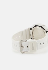 White silicone watch strap with a silver metal buckle, round case back, textured surface, and multiple adjustment holes.
