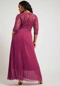 Pitkä luumunvärinen mekko, jossa on pitsinen bodice, kolmivartalohihan muotoilu, laskostettu hame ja avainaukko selkädetaili. Sujuva, virtaava rakenne.
