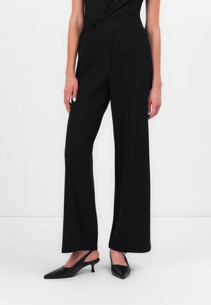 Black wide-leg pants made of smooth fabric feature an elastic waistband. Paired with pointed black heels. Simple, modern design.