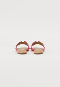 Open-toe sandals with bright pink straps and tan soles. Features a minimal design with cut-out accents and a flat profile.