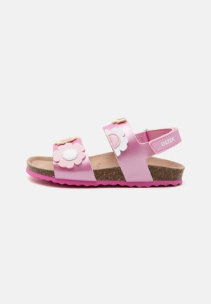 Pink sandals with flower accents, made of synthetic material, featuring cork footbed, adjustable straps, and textured sole. Geox branding visible.