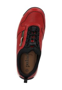 Zapatilla roja de cuero con acentos negros, que cuenta con una cremallera, cordones elásticos y una plantilla color beige. Diseño curvado con punta redonda y parte superior texturizada.