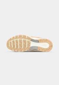 Semelle de chaussure de course Nike avec une surface en caoutchouc texturé, présentant des motifs carrés en beige, des accents blancs et un logo visible.