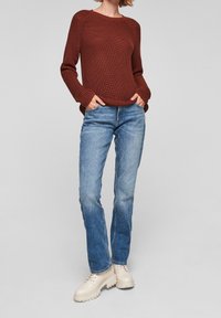 Gebreide sweater in roestkleur met geribbelde textuur, gecombineerd met lichtblauwe rechte jeans en beige veterlaarzen met een dikke zool.