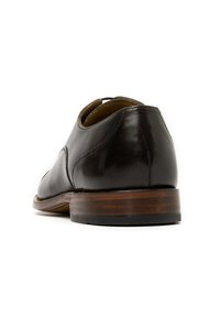 Scarpa in pelle marrone scuro con finitura liscia, dotata di tacco in legno e dettagli di cucitura sottili. Punta rotonda con accenti di design minimi.