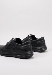 Zapatos de cuero negro con una textura suave, forma redondeada y diseño de cordones. Cuentan con una suela resistente y detalles de costura sutiles.
