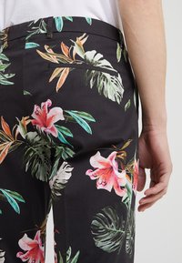 Schwarze Stoffhosen mit einem lebhaften Blumenmuster aus pinkfarbenen Lilien und grünen Blättern, taillierte Passform und einer einzelnen Gesäßtasche.
