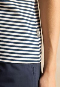 Tumesinine ja valge triibuline lühikeste varrukatega pluus, pehme puuvillane materjal, millel on hemperis väike "JOULES" silt, sile viimistlus ja lõdvestunud lõige.