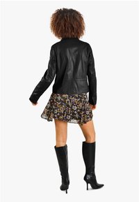 Černá kožená bunda s přiléhavým designem, zkombinovaná s květinovými šaty ve stylu skater. Modelka má na sobě černé vysoké lodičky do kolen.
