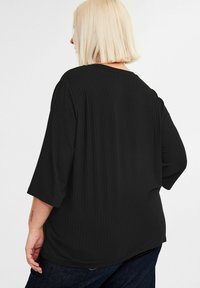 Schwarzes, geripptes, übergroßes T-Shirt mit dreiviertel Ärmeln, rundem Ausschnitt und glatter Textur, kombiniert mit dunkelblauen Jeans.