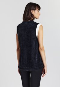 Top in maglina senza maniche di colore blu navy, con una texture morbida, caratterizzato da dettagli in maglina bianca lungo le spalle. Vestibilità comoda, design semplice senza decorazioni.