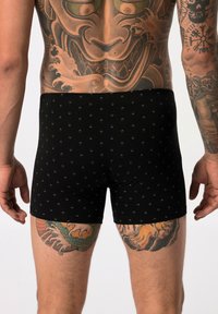 Boxer shorts noirs en tissu doux, avec un petit motif à flèches. La ceinture exposée est élastique et lisse.