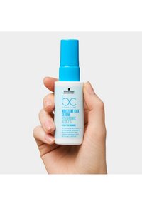 Bouteille blanche avec un bouchon bleu. Le texte indique "Sérum Hydratation Intense" et "Acide Hyaluronique 2 %". Main tenant la bouteille ; taille 50 ml.