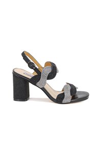 Sandal con tacco alto nero e argento, caratterizzata da una texture glitterata, cinturini ondulati e una tracolla regolabile con fibbia metallica.