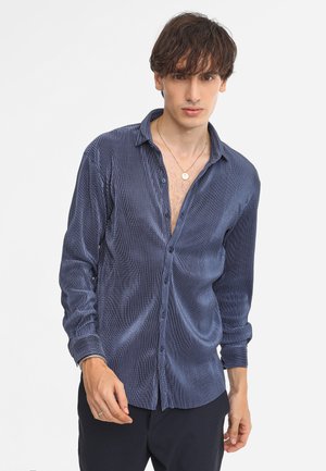 Camicia blu navy con bottoni, con fine motivo a righe verticali, tessuto leggero e colletto leggermente aperto. Maniche lunghe con polsini a bottone.