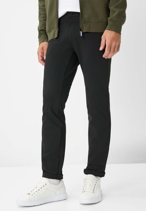 Schwarze stretchige Leggings mit schmaler Passform, mit einer glatten Textur und zwei seitlichen Taschen. Kombiniert mit weißen Turnschuhen für einen Kontrast.