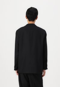 Schwarze Blazer mit klassischem Reversdesign, langen Ärmeln und geradem Schnitt. Der Stoff wirkt glatt, ohne sichtbare Muster oder Akzente.