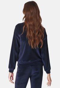 Felpa in velluto blu navy, vestibilità leggermente ampia, colletto rotondo, polsini e orlo ribattuti, abbinata a pantaloni coordinati, che mostrano una texture liscia.