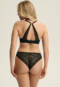 Czarny koronkowy stanik na ramiączkach z dekoltem w kształcie litery V i regulowanymi ramiączkami; pasujące koronkowe stringi z falbaniastymi brzegami. Miękki, skomplikowany wzór w kwiaty.