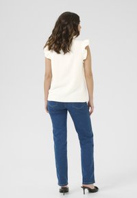 Haut sans manches blanc à côtes avec des accents de épaules froncés, associé à un jean droit bleu et des sandales à talons noires.