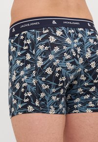 Námořnické modré boxerky s květinovým vzorem, který zahrnuje bílé květy a zelené listy. Elastický pas s logem 'JACK&JONES'.