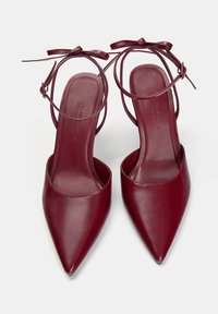 Burgundy klackar med spetsig tå och slät lädertextur. Utrustad med tunna justerbara ankelband och en slip-on design.