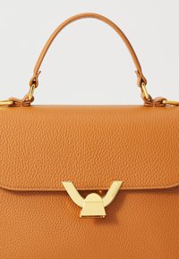 Borsa a mano in pelle beige con finitura texturizzata, dotata di un fermaglio dorato e di un manico corto. Design semplice senza ulteriori decorazioni.