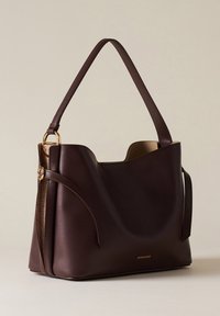 Braune Leder-Schultertasche mit geschwungenem Design, einem einzelnen Tragegurt, goldfarbenen Beschlägen und einer glatten Textur. Auffälliges seitliches Akzent.